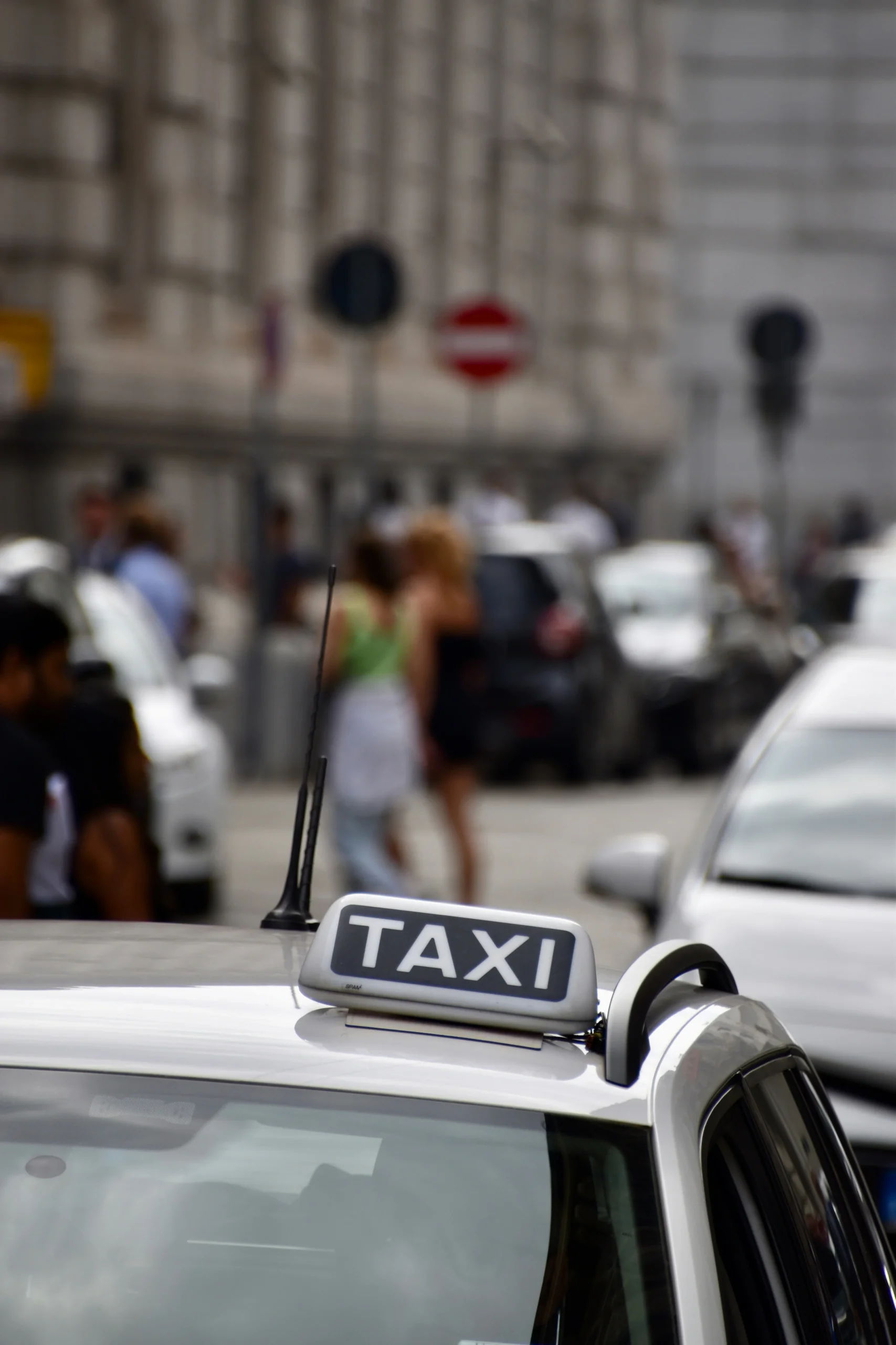 Сріблясте таксі з написом TAXI на даху серед людей на міській вулиці